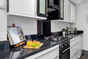 A modern kitchen with white cabinets, a black countertop, a built-in oven, and a coffee machine. - Chorlton House | Free Parking | 2BR Stoke-on-Trent (Stoke-on-Trent)