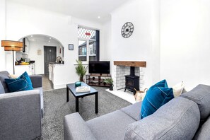 A modern living room with grey sofas, a coffee table, a fireplace, and a TV.