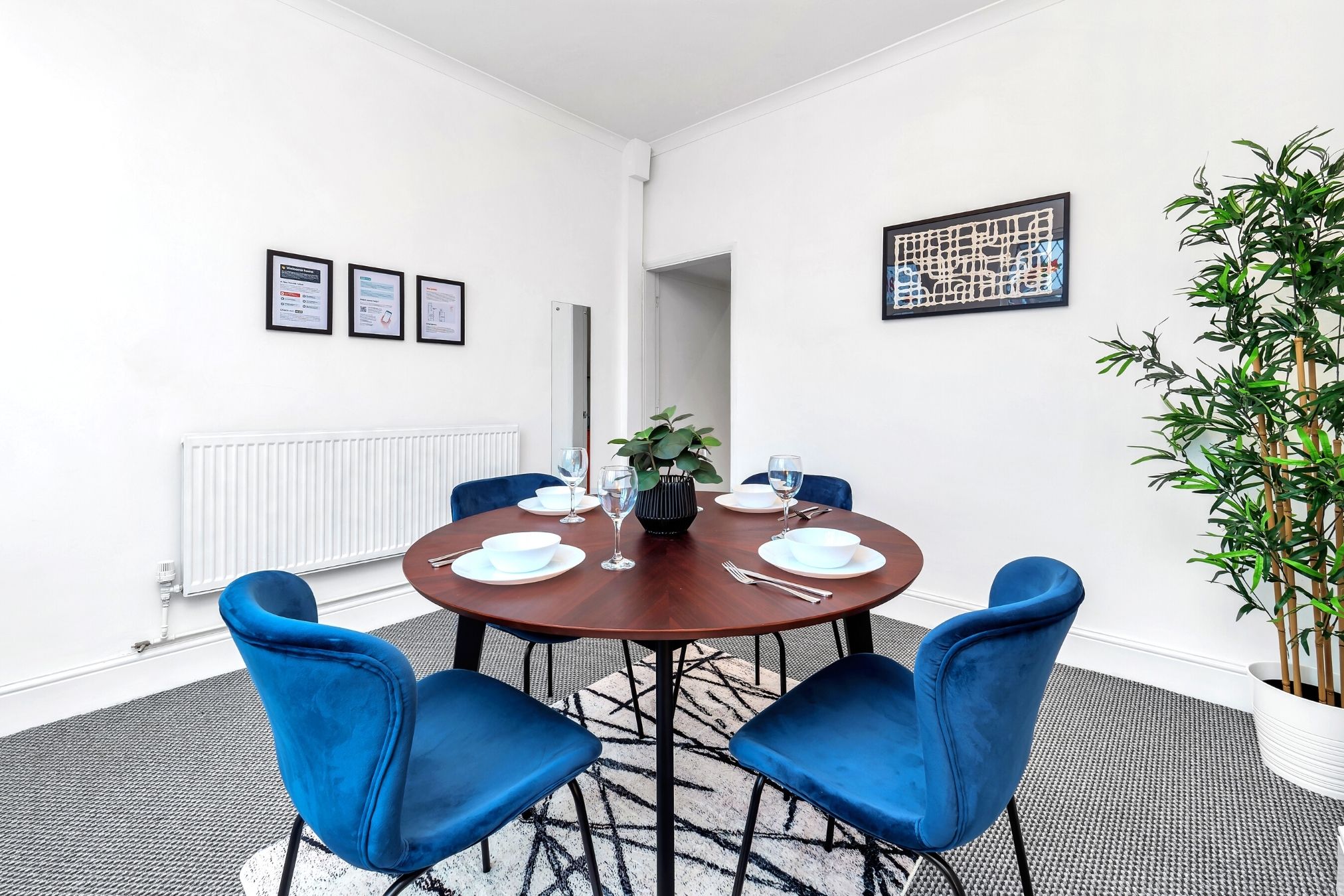 A conference room with a round table, four blue chairs, a potted plant, and framed certificates on the wall.