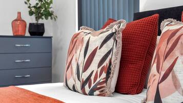 A bedroom with a bed, pillows, a dresser, a vase, and a plant.