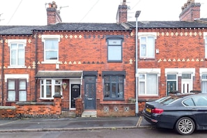 A row of red brick terraced houses with front doors, windows, and a parked car.