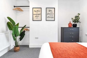 A modern bedroom with a bed, a dresser, a radiator, a potted plant, and two framed inspirational quotes on the wall. - Chorlton House | Free Parking | 2BR Stoke-on-Trent (Stoke-on-Trent)
