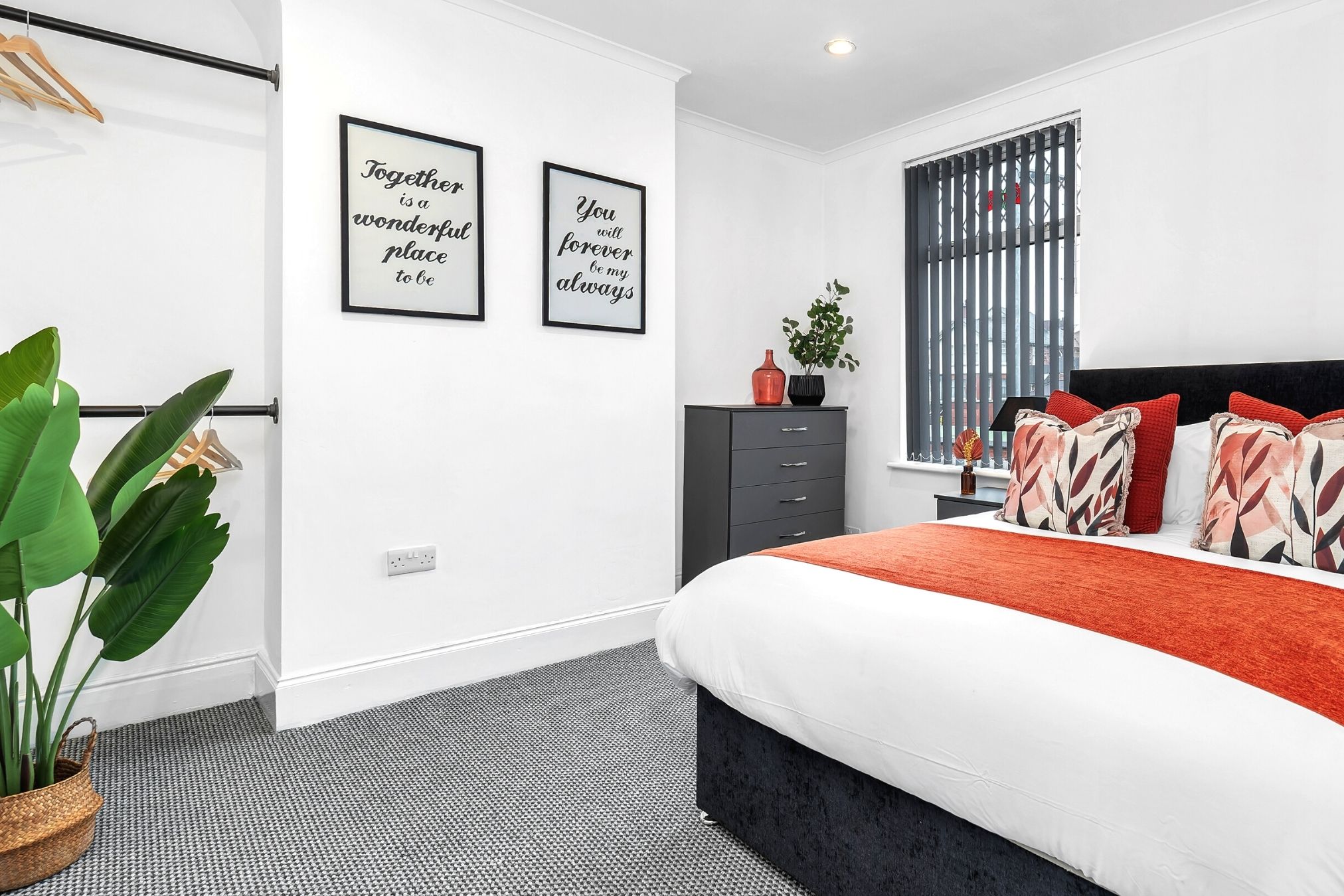 Un dormitorio moderno con una cama, un aparador y dos carteles con mensajes inspiradores en la pared.