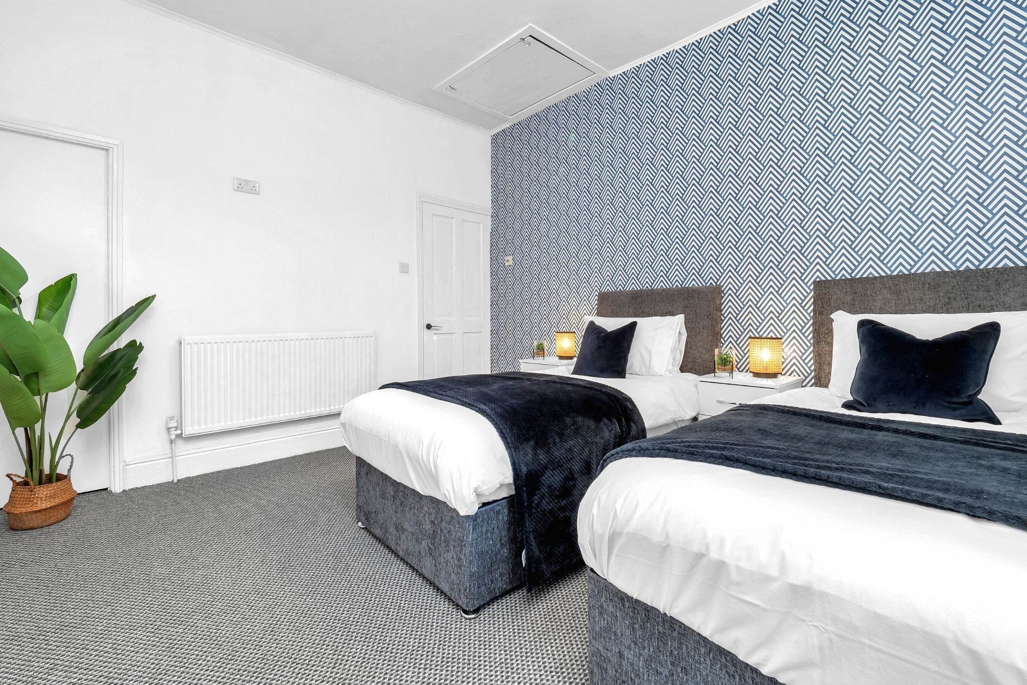 Habitación de hotel moderna con dos camas, una planta en maceta grande y una pared con diseño.