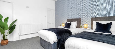 Habitación de hotel moderna con dos camas, una planta en maceta grande y una pared con diseño.