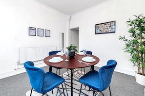Une salle de conférence avec une table ronde, des chaises bleues, une plante en pot, des certificats encadrés et un radiateur.