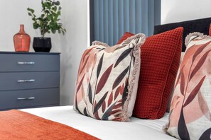A bedroom with a bed, pillows, a dresser, a vase, and a plant.