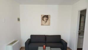 Uma sala de estar com um sofá escuro, uma mesa de centro de vidro e um quadro na parede.