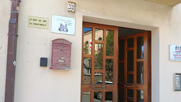A building entrance with a wooden door, a mailbox, and several signs on the wall. - AT THE OLD STUDIO (Vibo Valentia)