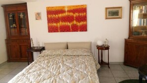 A bedroom with a bed, a wooden cabinet, a small table with a lamp, and a painting on the wall. - AT THE OLD STUDIO (Vibo Valentia)