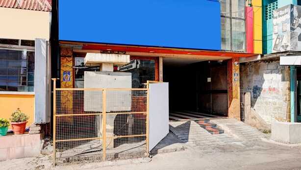 Un edificio con toldo azul, entrada protegida por una reja y una escalera que conduce a un espacio cubierto.
