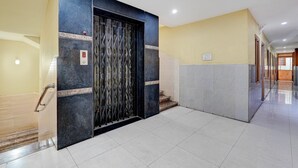 Un pasillo con un ascensor negro, piso de baldosas y pared amarilla.