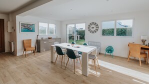 Un comedor amplio con una mesa y sillas blancas, ventanas grandes y vistas al exterior.