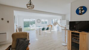 Un salón amplio con una televisión grande, suelo de madera y una zona de comedor con luz natural.
