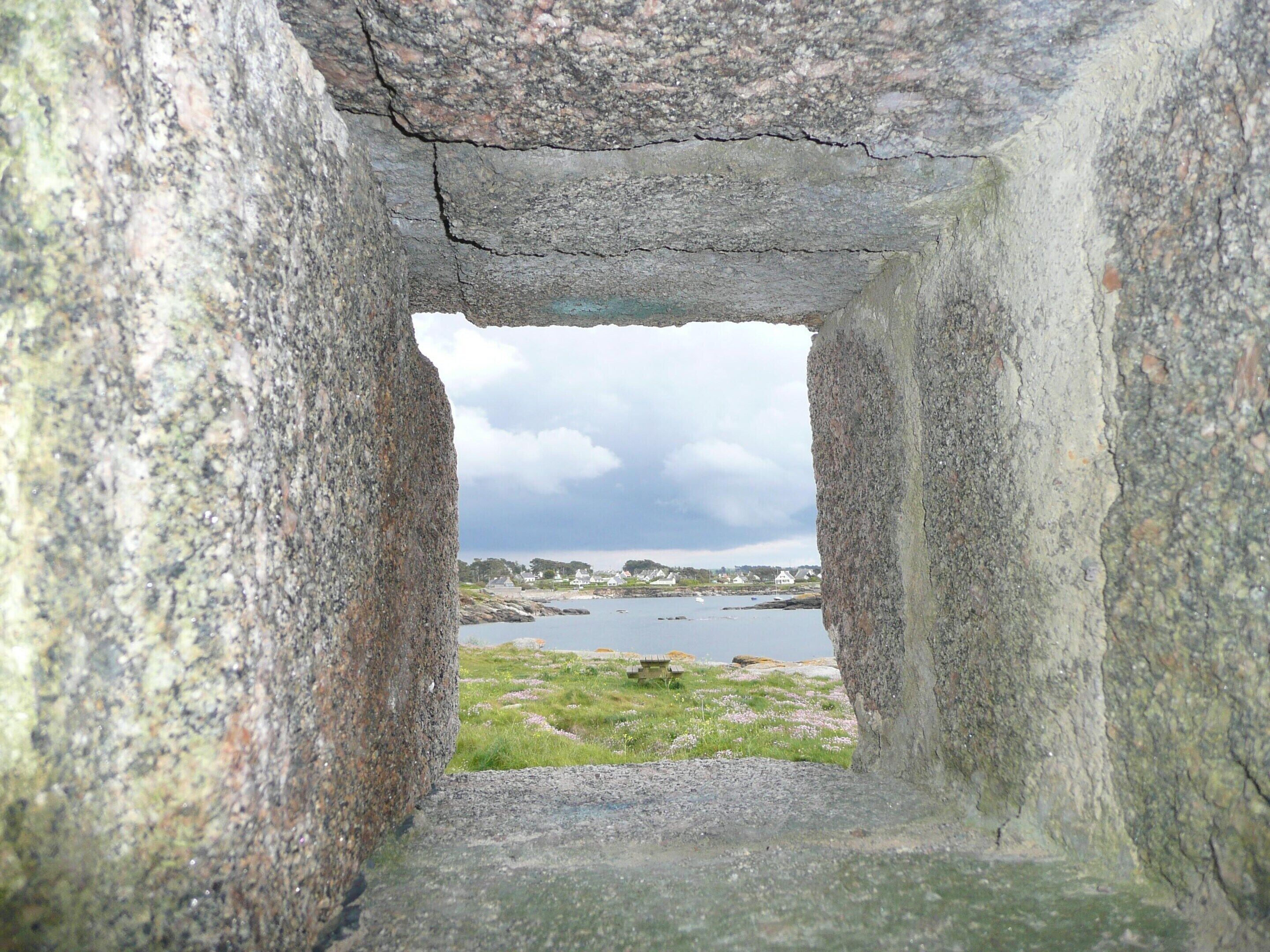 Een gebouw van steen met uitzicht op een kustlandschap, inclusief een waterpartij en verre gebouwen.