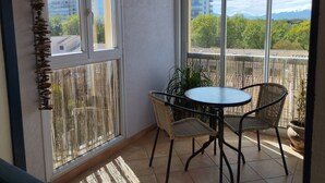 Ein Balkon mit Tisch und Stühlen, einem Blumentopf und Blick auf Gebäude und Bäume.