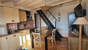 Eine Küche mit Holzschränken, einem Esstisch mit Stühlen, einer Hängelampe und einer Treppe, die zu einer weiteren Ebene führt.