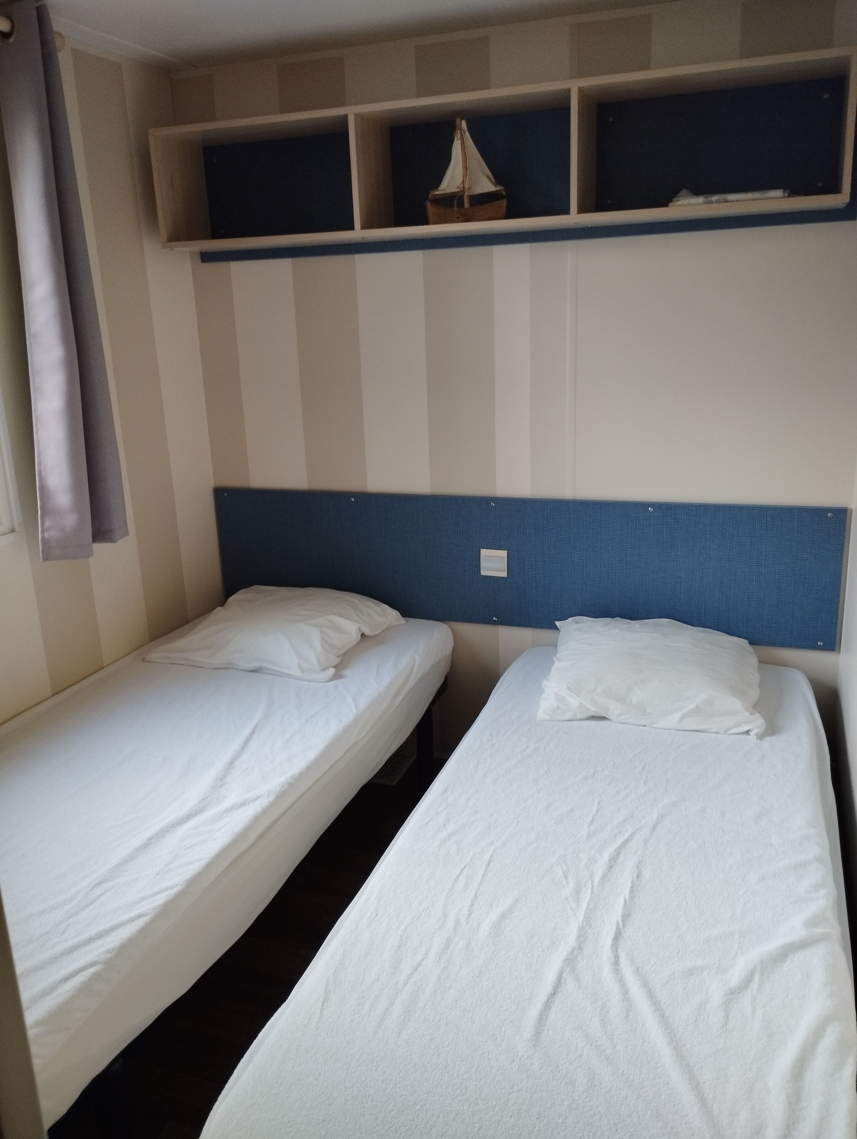 Una habitación con dos camas individuales, cabeceros y un estante sobre las camas.