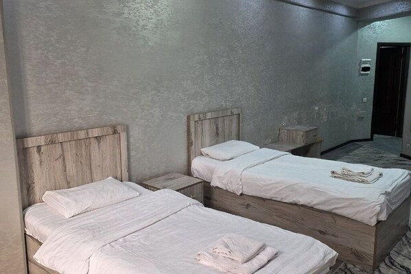 A room with two wooden beds, each with white bedding and pillows, and a small wooden nightstand beside each bed. - Sarvat Hotel (Dushanbe)