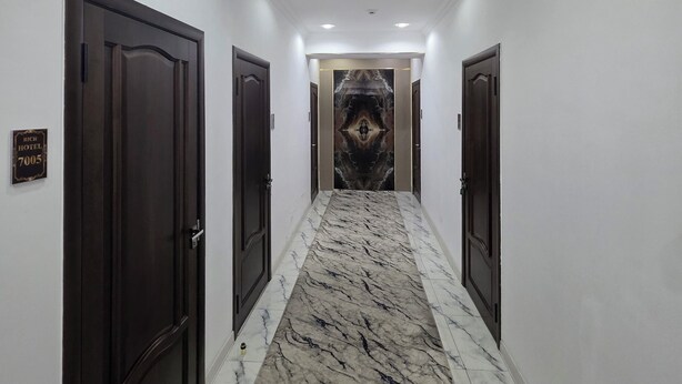 A hallway with marble flooring, dark wooden doors, and a central wall with a decorative pattern. - Sarvat Hotel (Dushanbe)