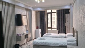 A hotel room with two beds, a flat-screen TV mounted on the wall, a small shelf with toiletries, a window with curtains, and a marble-patterned floor. - Sarvat Hotel (Dushanbe)