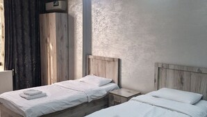 A room with two beds, a wooden wardrobe, and a small bedside table. - Sarvat Hotel (Dushanbe)
