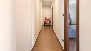 A long, narrow hallway with a wooden floor and white walls. - Panoramic Rooms  (Syracuse)