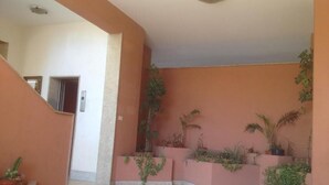 A spacious indoor area with a tiled floor, a staircase on the left, and several planters with various plants. - Panoramic Rooms  (Syracuse)