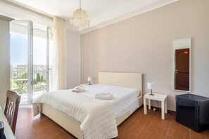 A hotel room with a large bed, a small bedside table with a lamp, a TV, and a balcony with a view of the city. - Panoramic Rooms  (Syracuse)