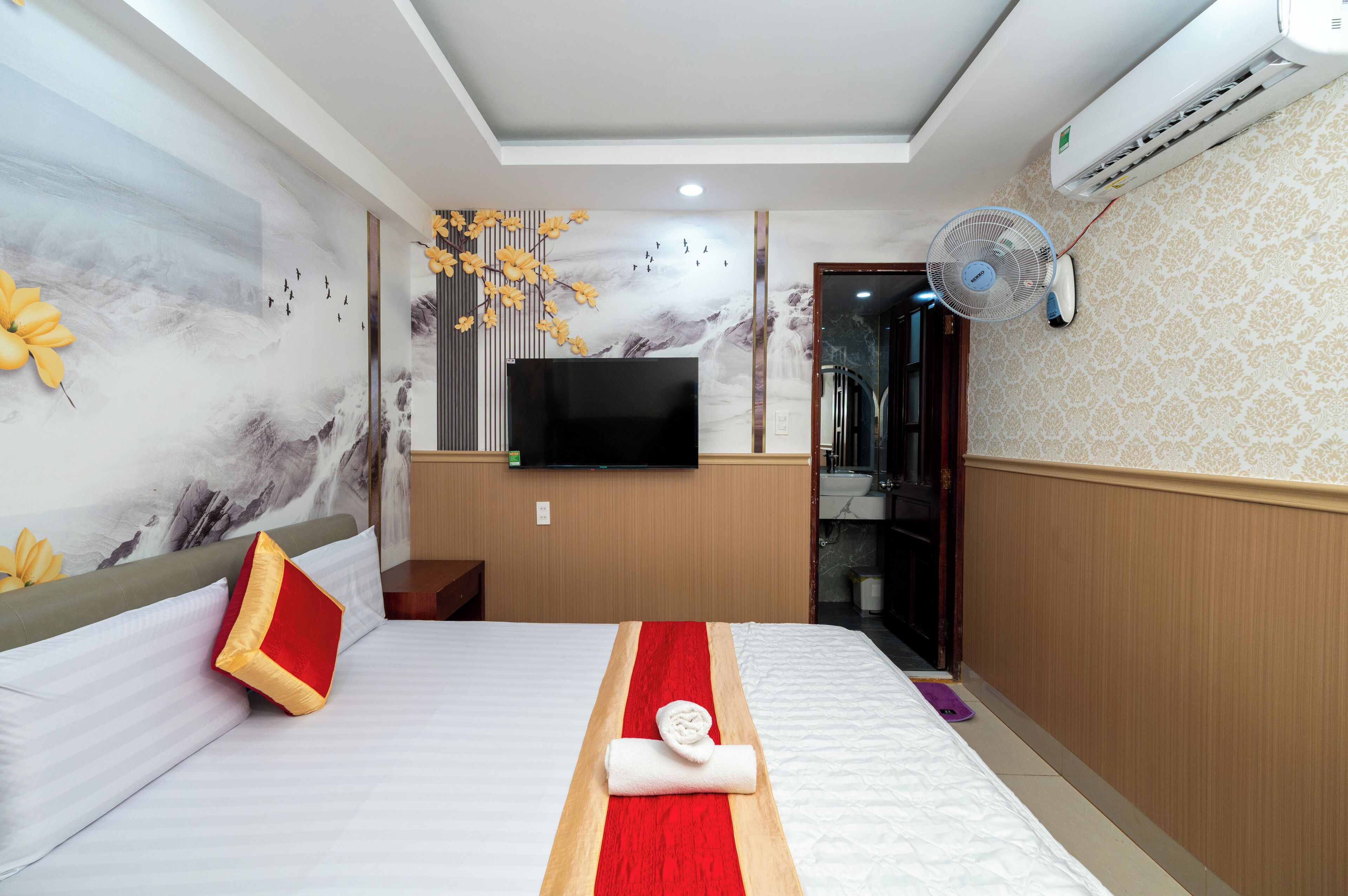 A hotel room with a bed, a flat-screen TV, a wall-mounted air conditioner, and a bathroom visible through an open door.