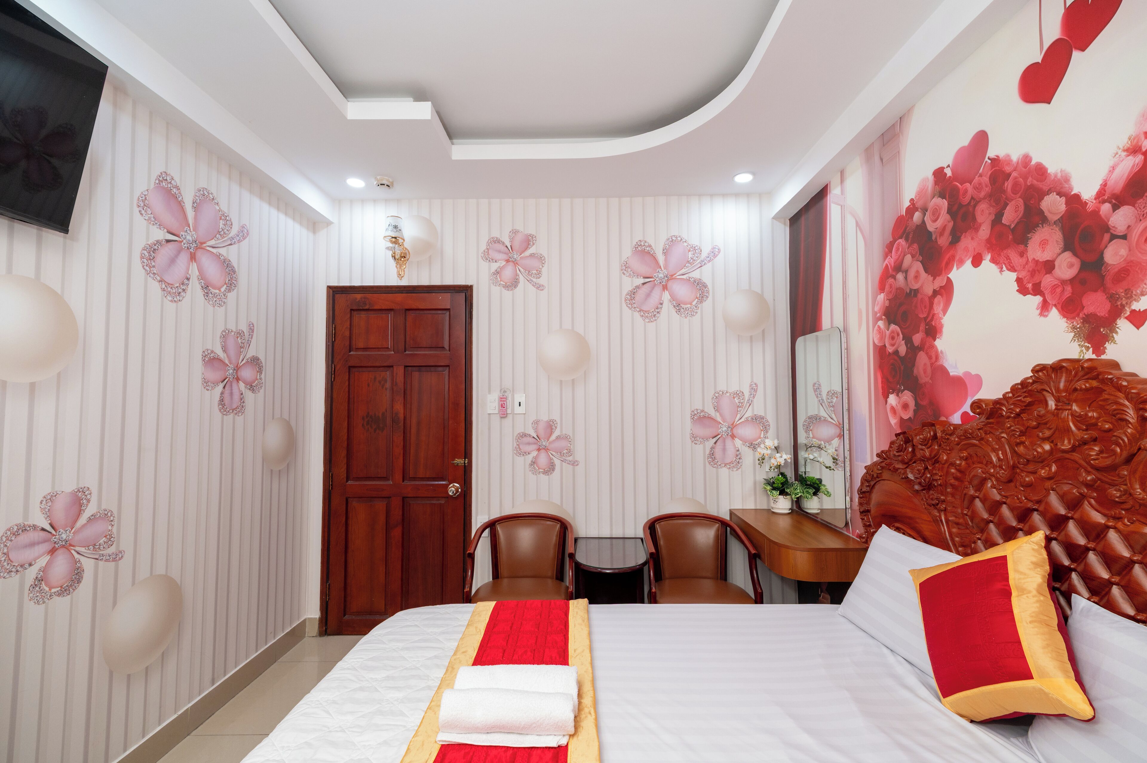 A hotel room with a bed, two chairs, a small table, a TV, and decorative wall art.