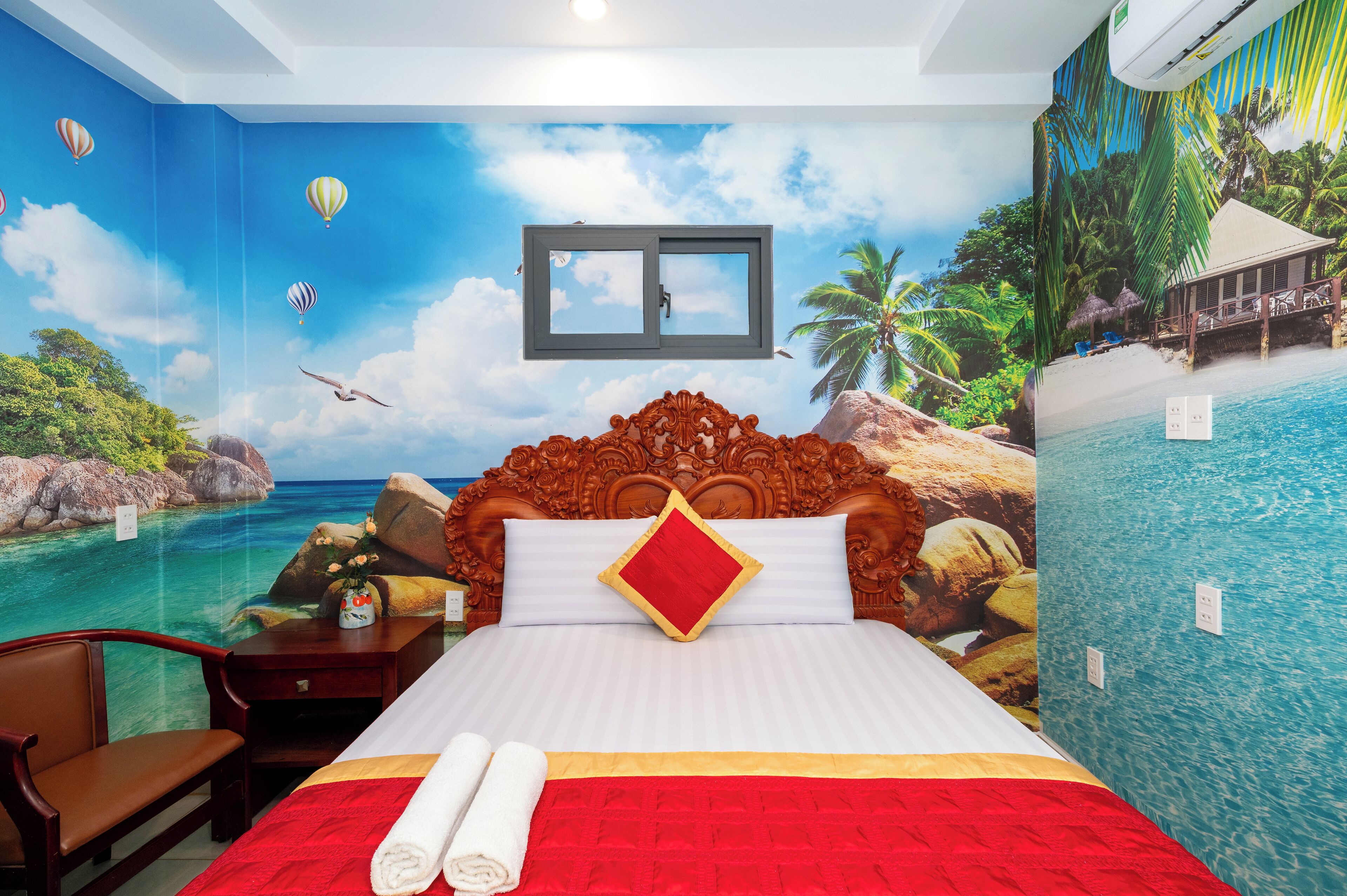 A bedroom with a large bed, a wooden headboard, a nightstand, a chair, and a wall mural of a beach scene.