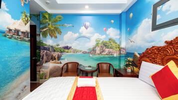 Hotelkamer met een muurschildering van een tropisch strand, een bed met een rood-witte plaid, twee stoelen en een kleine tafel.