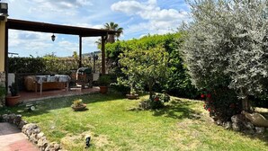 A patio area with a table and chairs, surrounded by a garden with various plants and a pergola structure. - Sunny Sicilian Apartment with Garden & Deck (Caltanissetta)