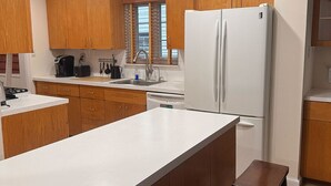 A kitchen with wooden cabinets, a white countertop, a white refrigerator, and a wooden bench. - Cozy Expanded Rambler in Bethesda - Nature Retreat (Bethesda)