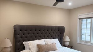 A bedroom with a tufted headboard, a bed with white linens, two bedside lamps, and a window with blinds. - Cozy Expanded Rambler in Bethesda - Nature Retreat (Bethesda)