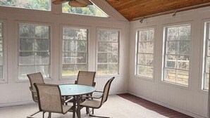 A room with a wooden ceiling, large windows, a table with chairs, and a ceiling fan. - Cozy Expanded Rambler in Bethesda - Nature Retreat (Bethesda)