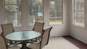 A sunroom with a ceiling fan, a round table with chairs, and large windows. - Cozy Expanded Rambler in Bethesda - Nature Retreat (Bethesda)
