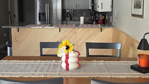 Una cocina moderna con electrodomésticos de acero inoxidable, un comedor con mesa y sillas de madera, y una isla de cocina con un jarrón de girasoles.