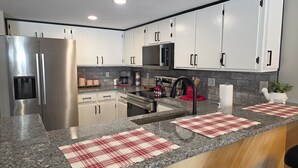 Una cocina moderna con electrodomésticos de acero inoxidable, armarios blancos, encimeras de granito y una alfombrilla a cuadros rojos y blancos.