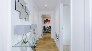 A modern hallway with a glass table, a white door, and a dining area in the background. - 2BDR | Free Parking | Stylish Liverpool Apartment (Liverpool)