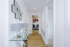 A modern hallway with a glass table, a white door, and a dining area in the background. - 2BDR | Free Parking | Stylish Liverpool Apartment (Liverpool)