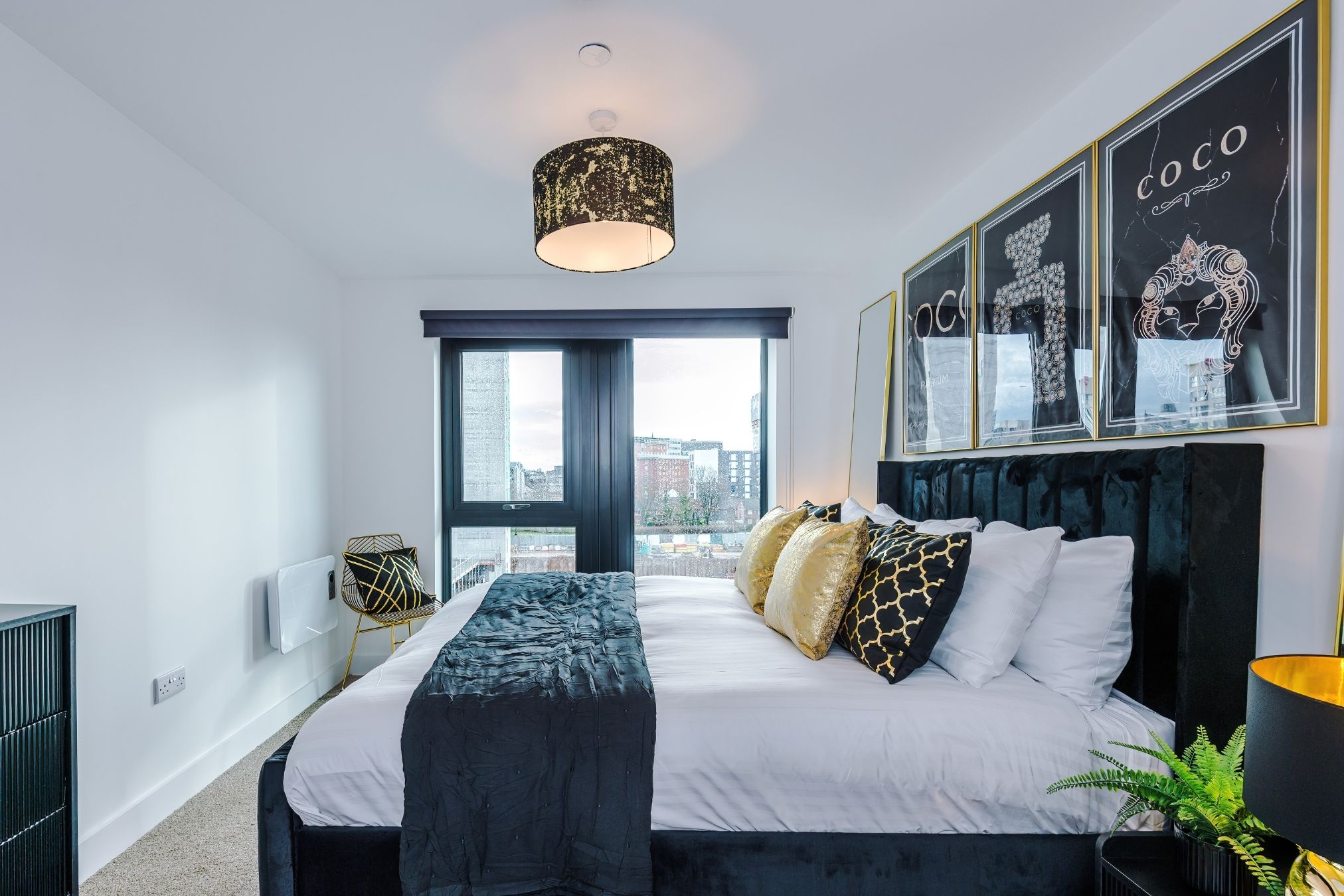 Een moderne slaapkamer met een groot bed, uitzicht op de stad en kunstwerken in lijsten aan de muur.