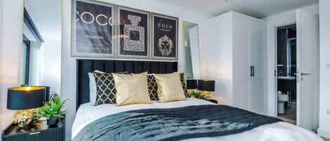 A modern bedroom with a large bed, a nightstand, a mirror, and framed artwork on the wall.