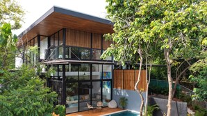 Una casa moderna de dos pisos con fachada de vidrio, terraza de madera y piscina.