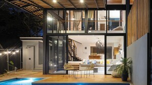 Una casa moderna de dos pisos con fachada de vidrio, una piscina y una escalera que conduce al nivel superior.