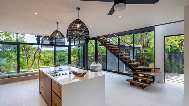 Una cocina moderna con una isla central, ventanas amplias y una escalera de madera.