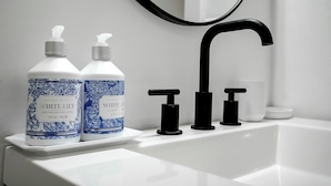 Un baño con dos botellas de loción hidratante para manos White Lily de Leucadia Bath Co., un grifo negro y un espejo.