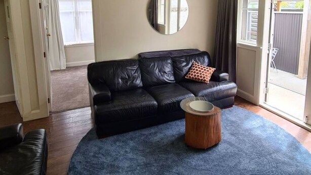 Ein Wohnzimmer mit einer schwarzen Ledersofa, einem runden Holztisch und einem blauen Teppich.