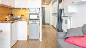 A compact kitchen with a microwave, toaster, and dishwasher, a grey sofa with a red pillow, and a wooden ceiling. - Cozy Mountain Base Near Bachat Bouloud (Chamrousse)